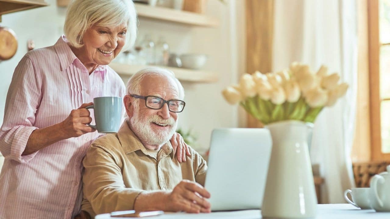 A senior couple happily looks at a tablet together in a bright kitchen.
