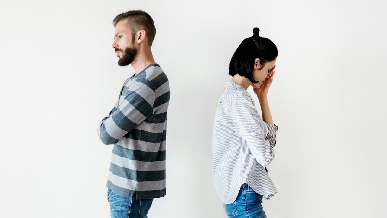 Man and woman standing back-to-back, looking upset.
