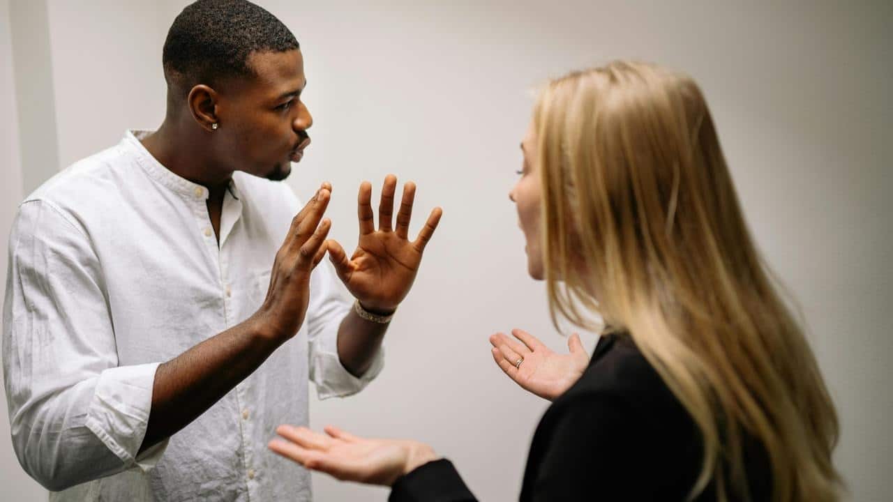A couple arguing face-to-face, both gesturing with frustration.
