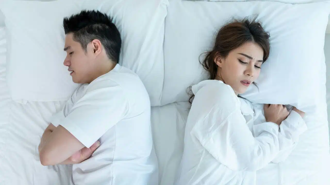 Overhead view of a couple lying in bed back-to-back, both looking distressed.