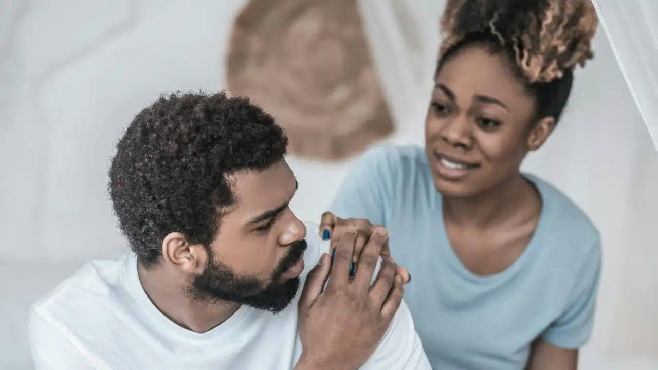 A woman apologizing to a man who is holding her hand to reassure her.