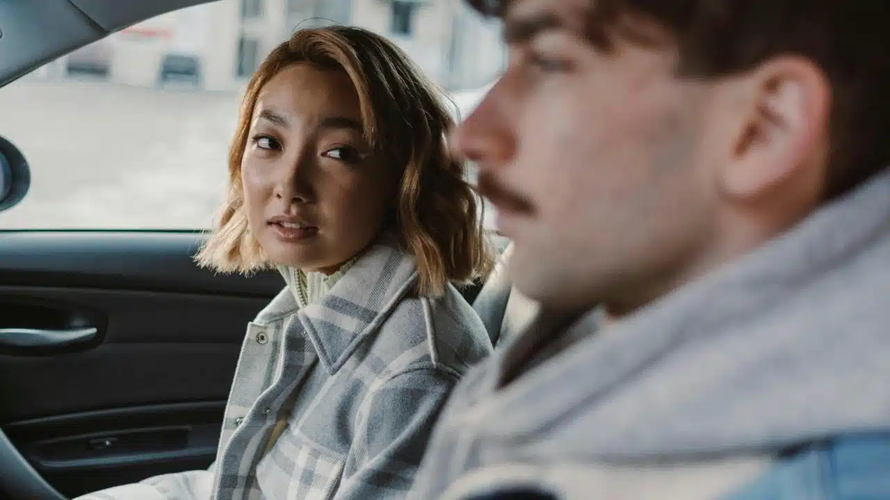 A woman sitting in a car looking at a man beside her.