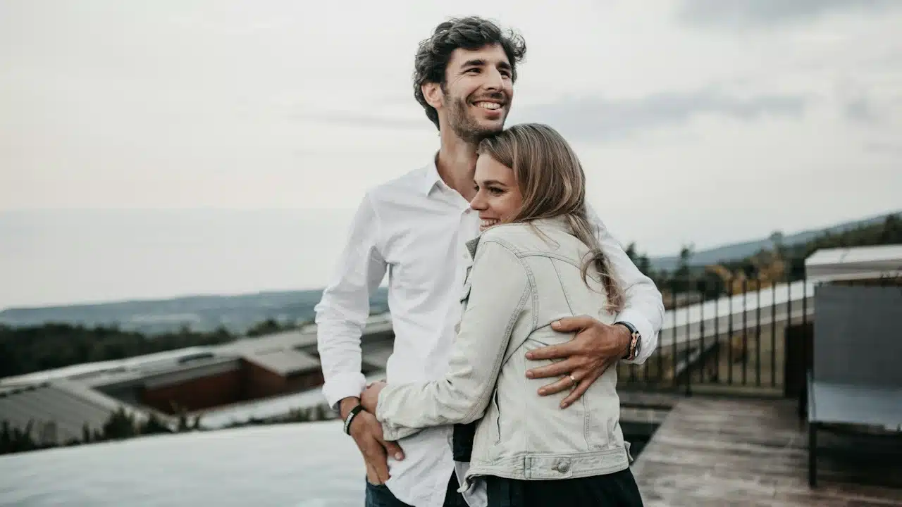 A smiling couple hugging each other while standing on the top of a building
