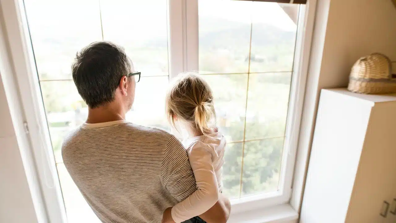 A man holds a child while looking out a window.