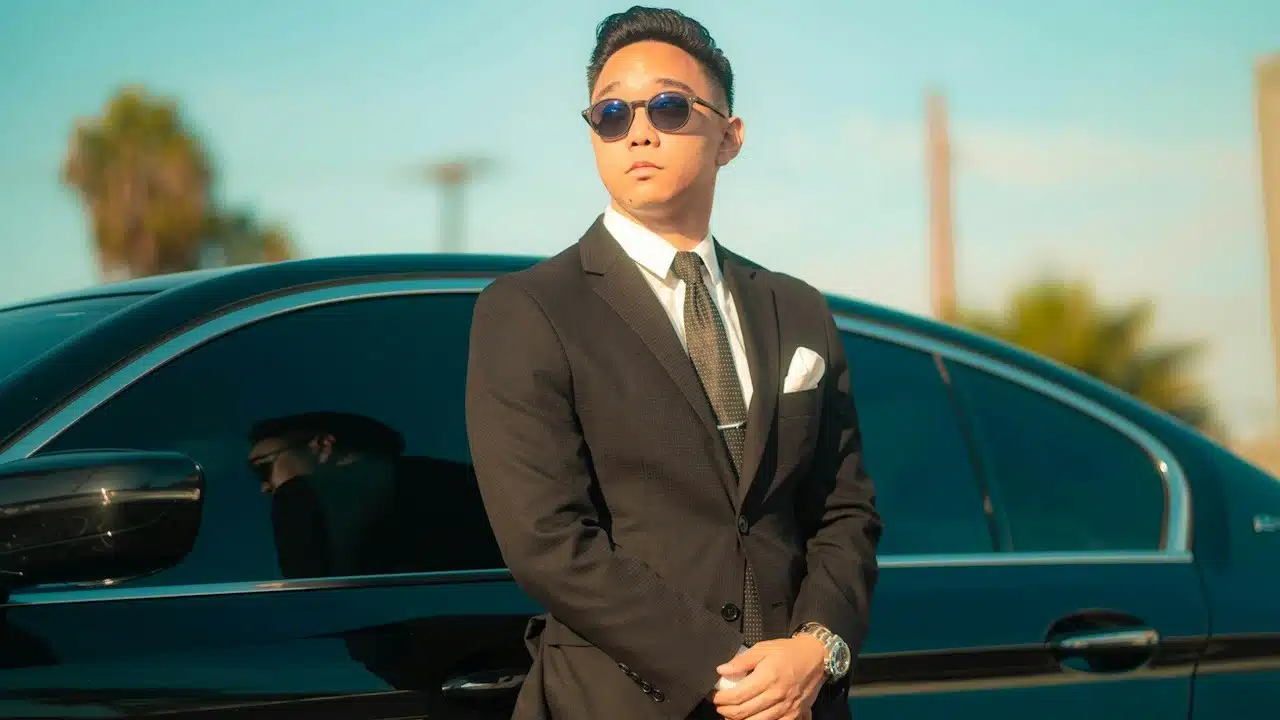 A young and confident man standing in front of his new luxury car.