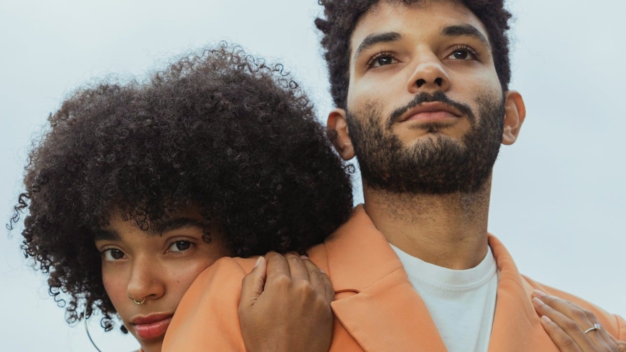 A woman with curly hair hugging a man from the backside.
