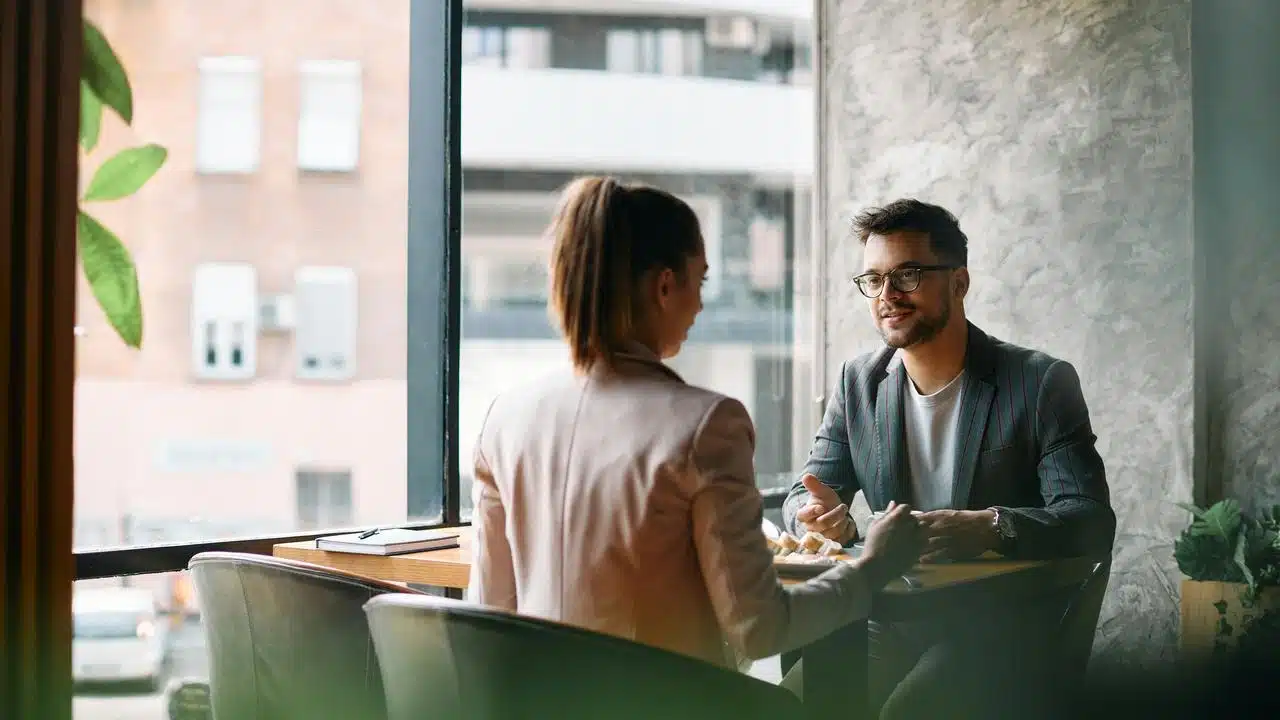A man and woman talking across a café table.