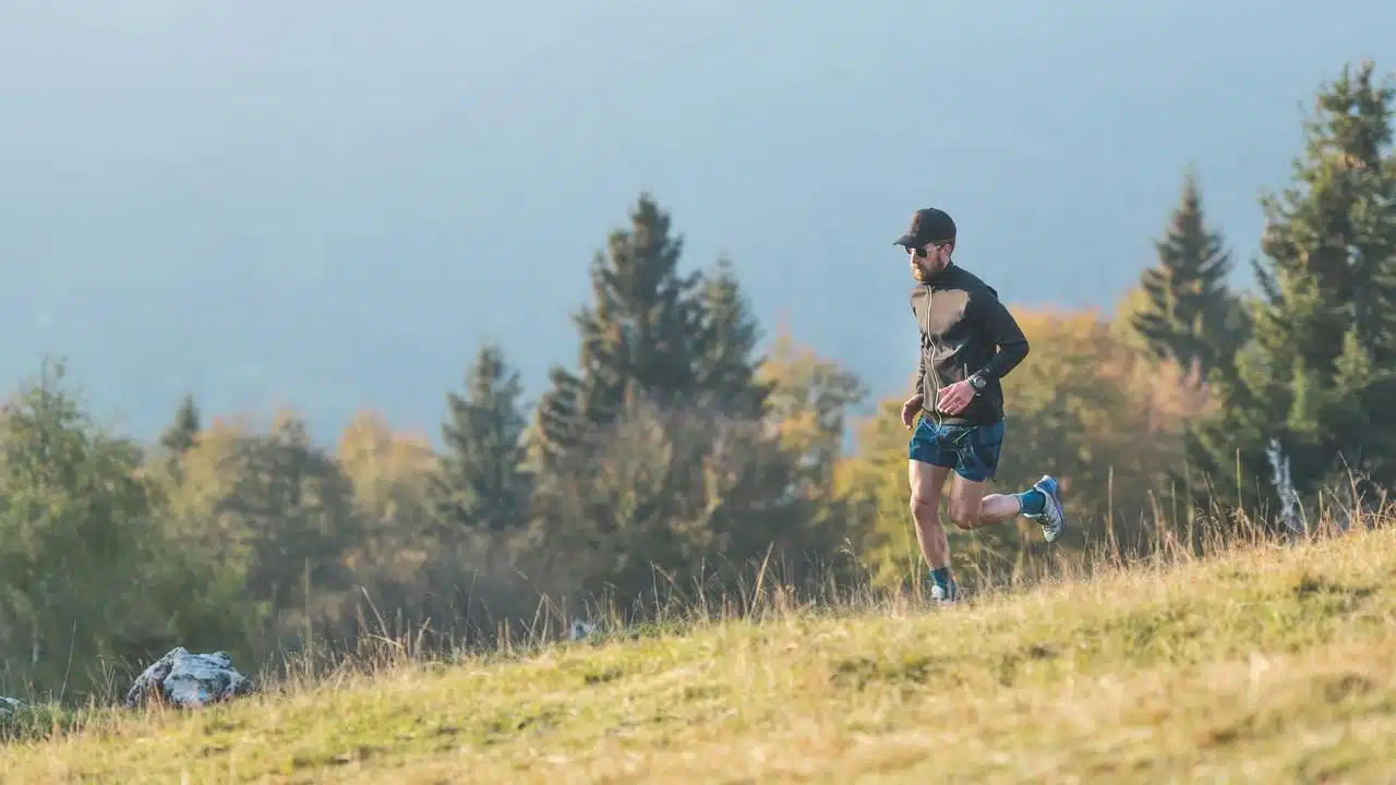 A man running on a grassy hill with trees in the background.