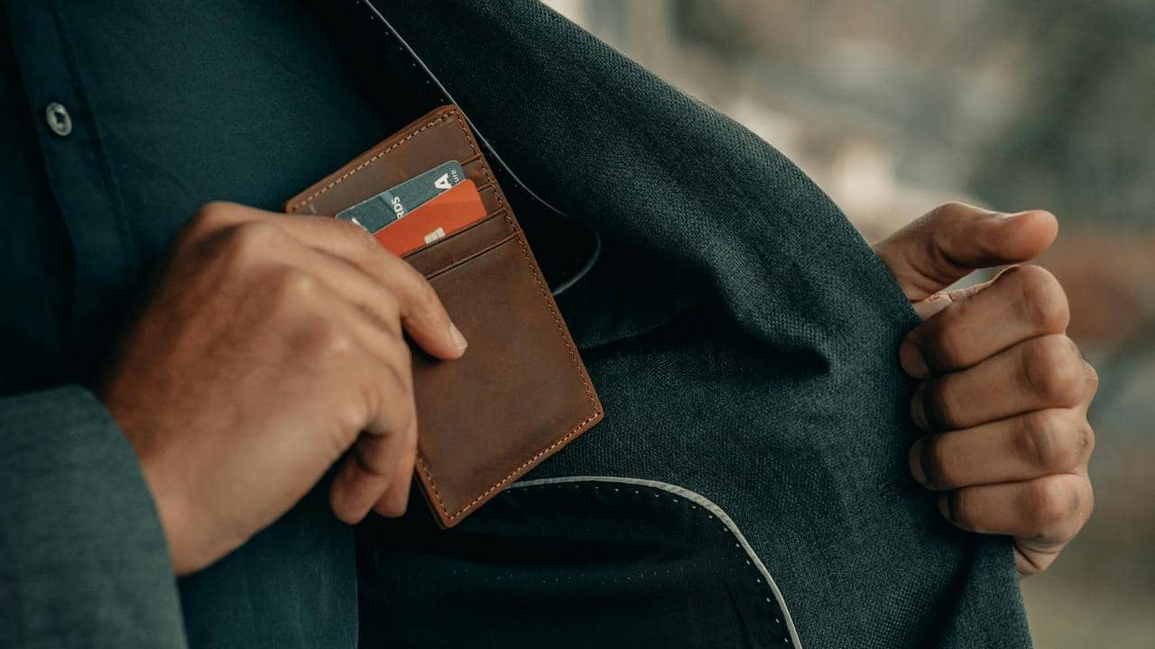 A slim brown leather cardholder being placed into a jacket pocket.