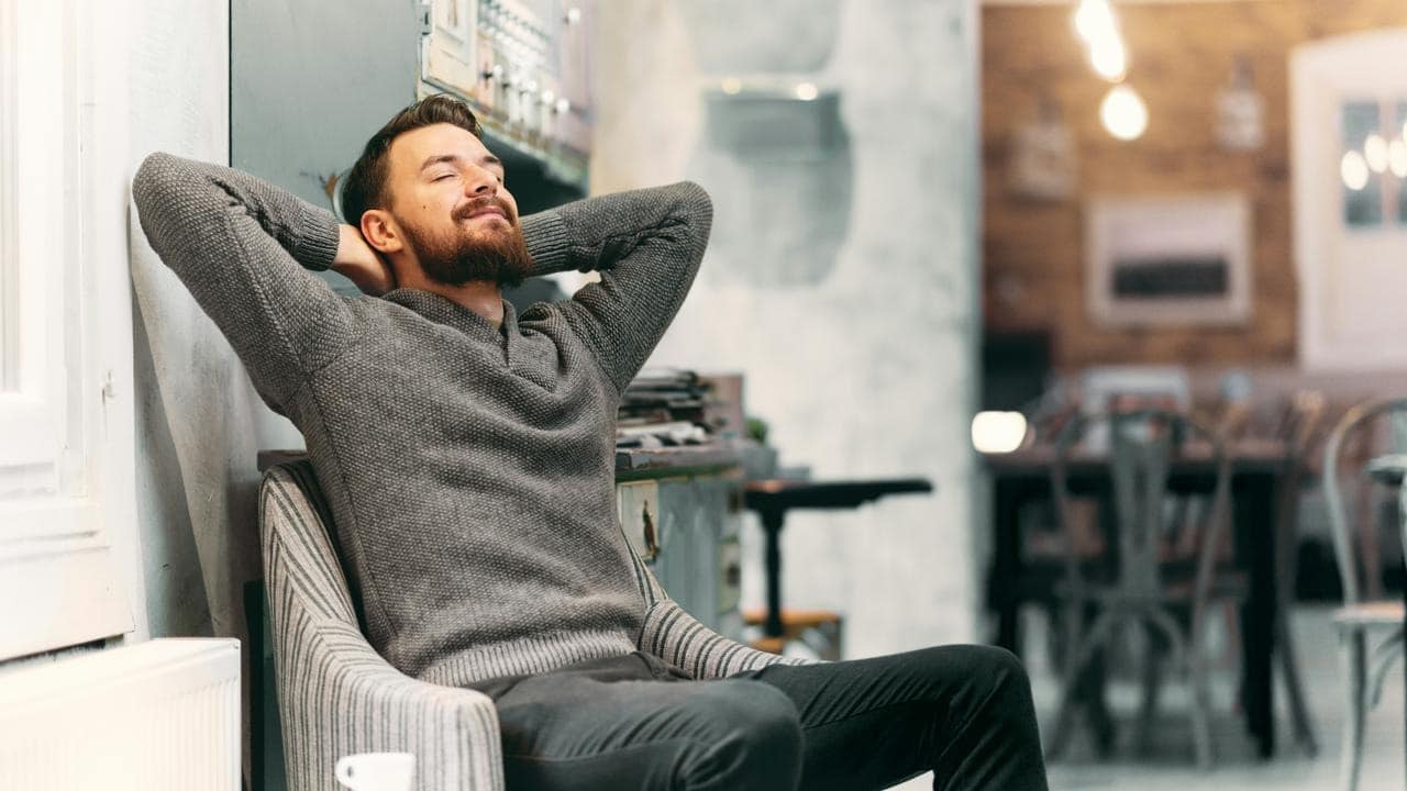 A bearded man leaning back in a chair with his hands behind his head.
