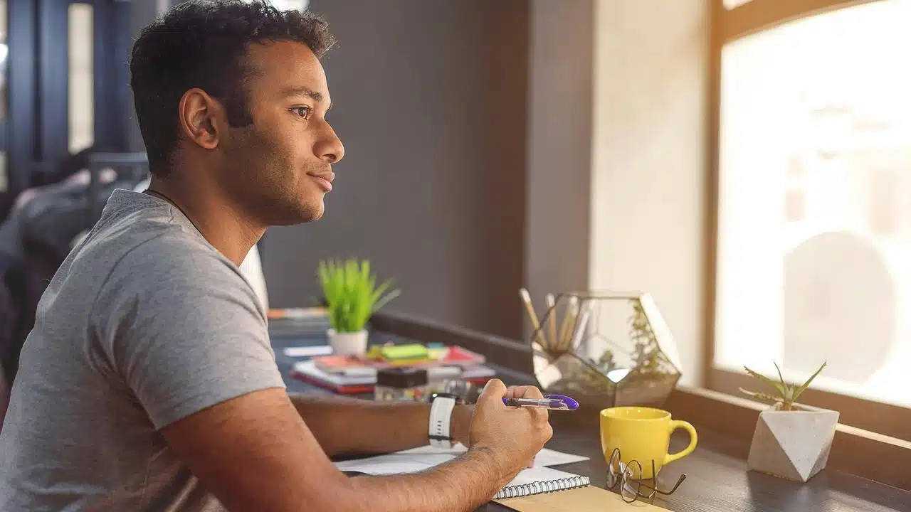 A man at a desk holding a pen while gazing out a window.