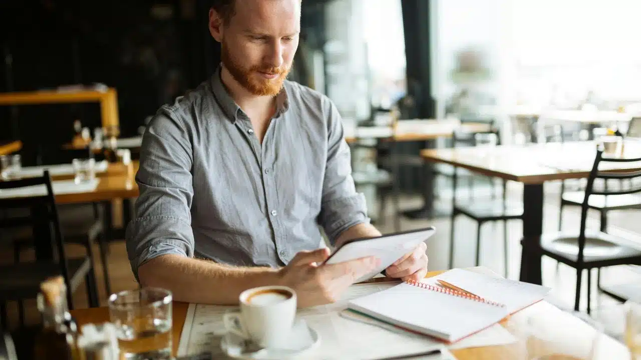 A bearded man using a tablet at a café table.