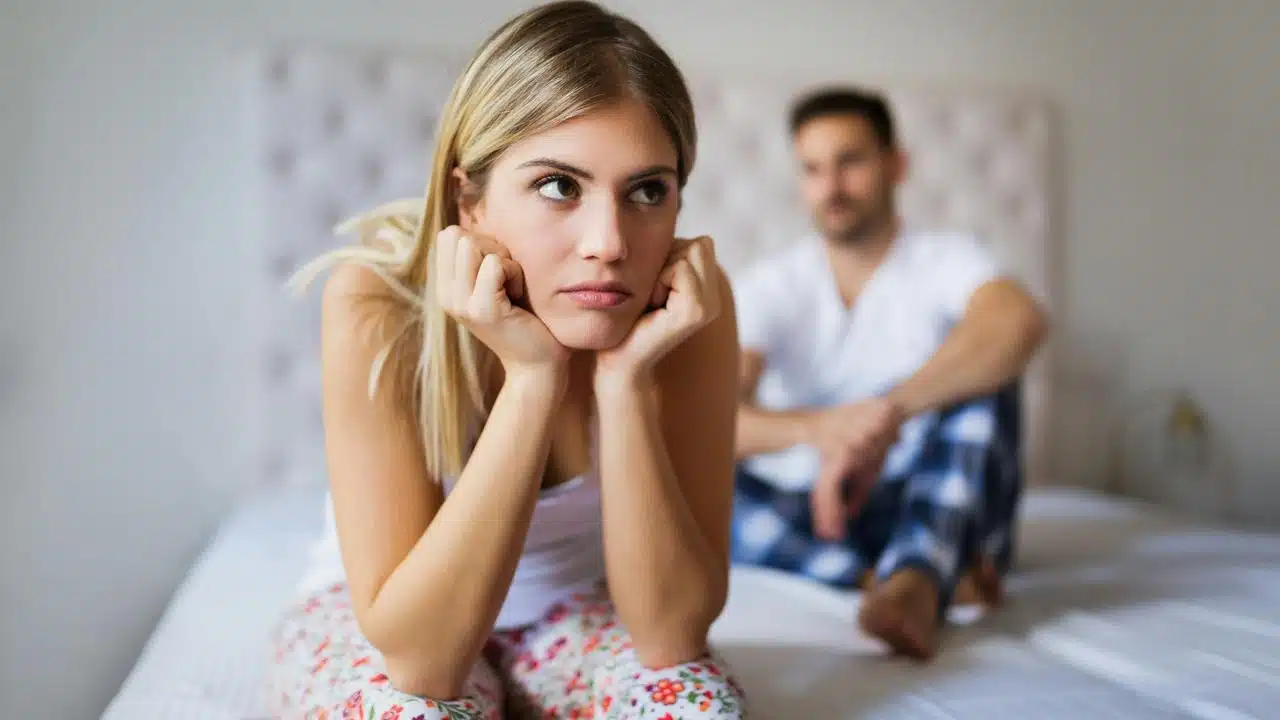 A woman looking upset on a bed with a man sitting behind her.