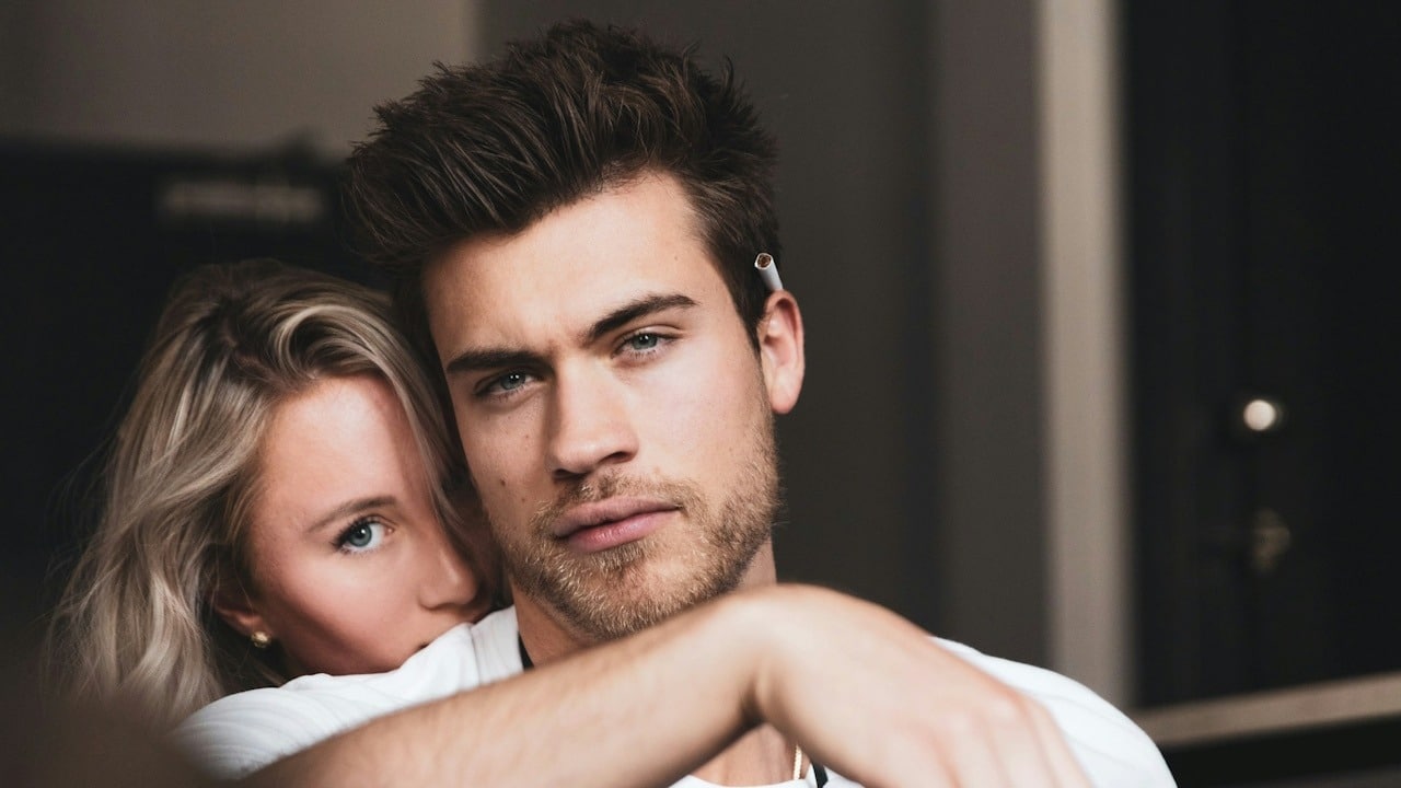A woman holding a bearded man tightly while he looks bored.