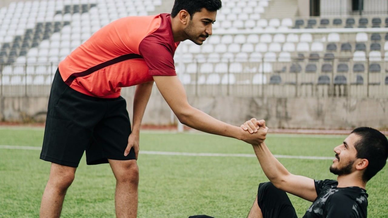 A man is helping another man get up while playing soccer.