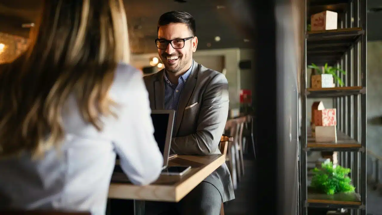 A man in glasses smiling at a woman across a cafe table.
