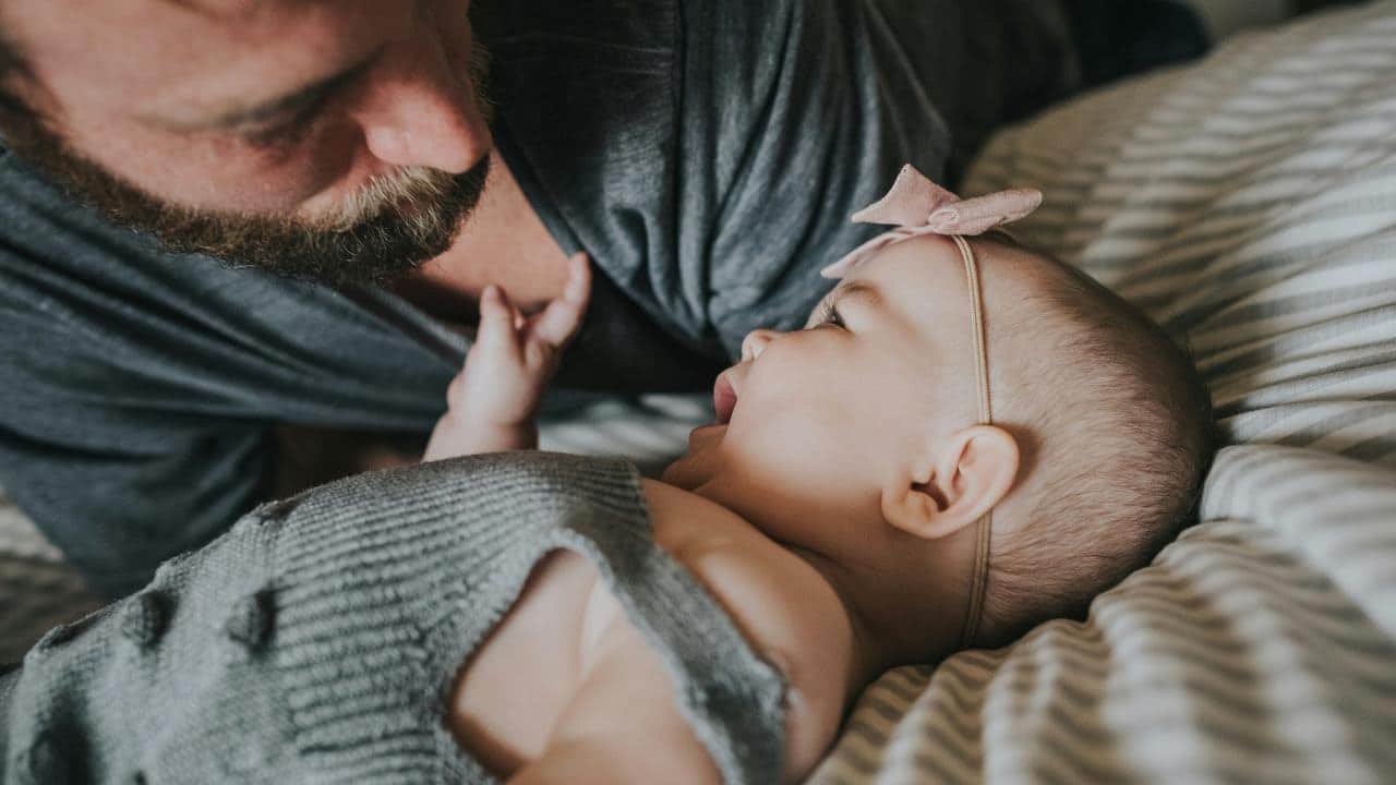 A man looking at a baby on a bed.