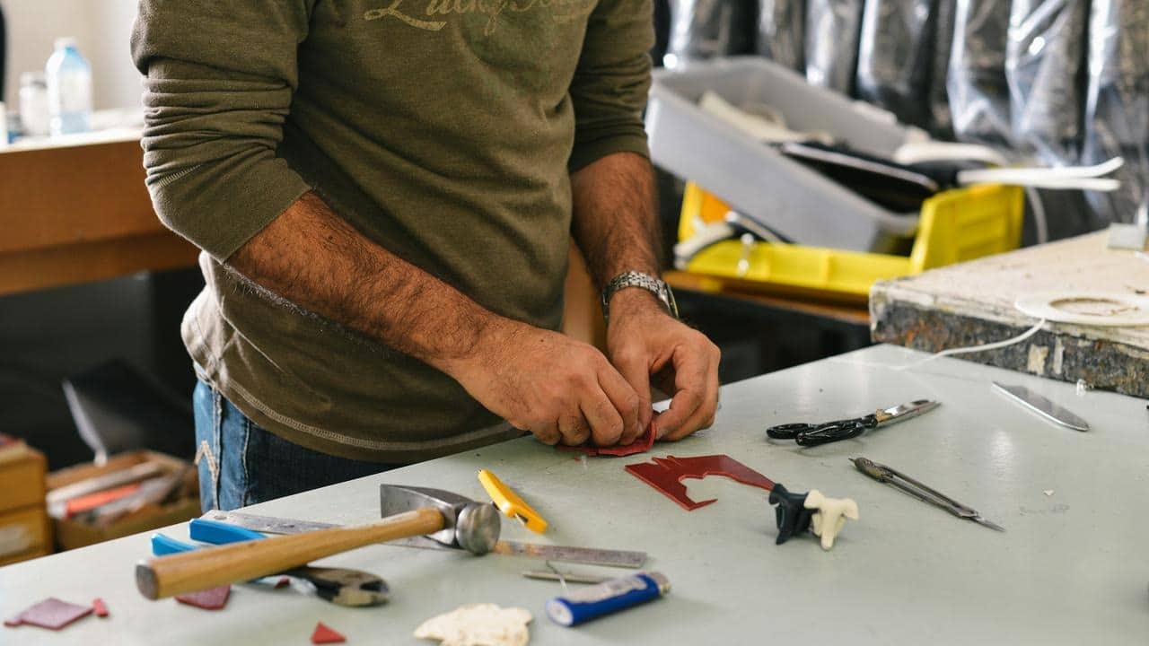 A person crafting red material on a tool-covered workbench.