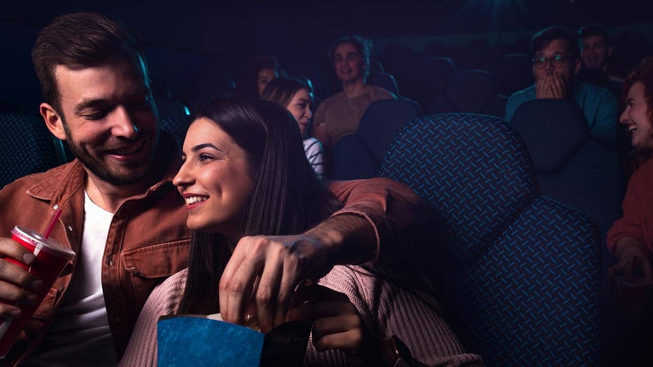 A couple sharing popcorn in a dark movie theater.
