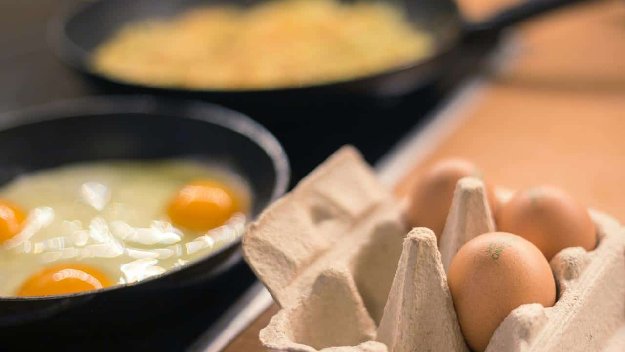 An egg carton beside eggs frying in a skillet.