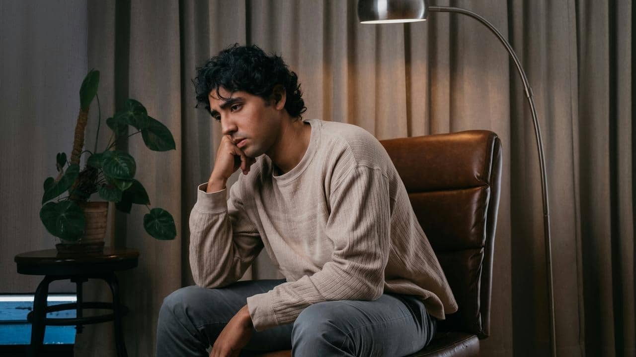 A worried young man sitting in a chair with his hand on his chin.
