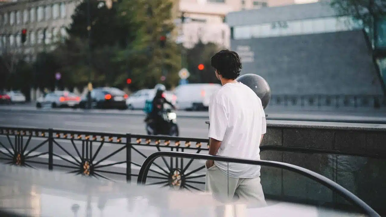 A man in a white shirt standing by a railing on a city street.