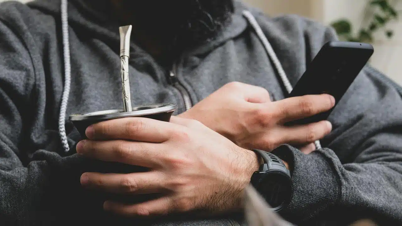 A person holding a mate gourd and a smartphone.