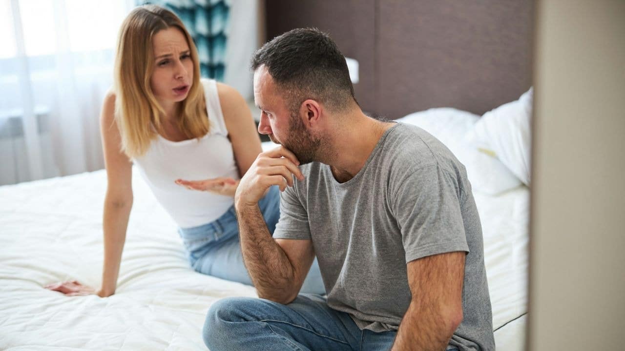 Man sitting with a concerned expression while a woman gestures and talks in the background.