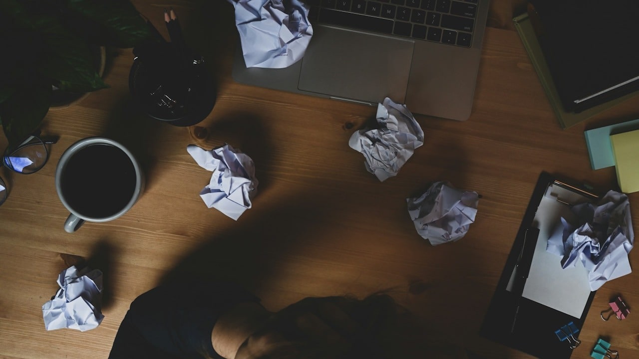 A stressed man surrounded by crumpled papers.