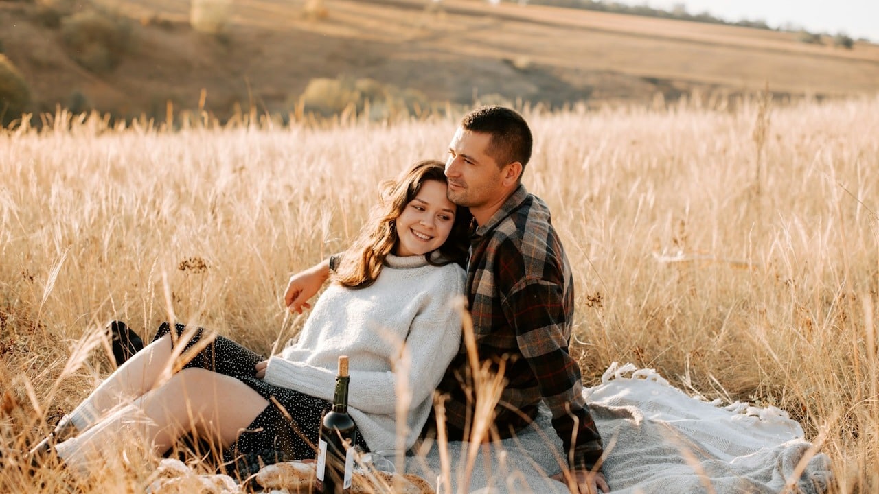 A woman laying in the lap of her husband while they are sitting in a field.