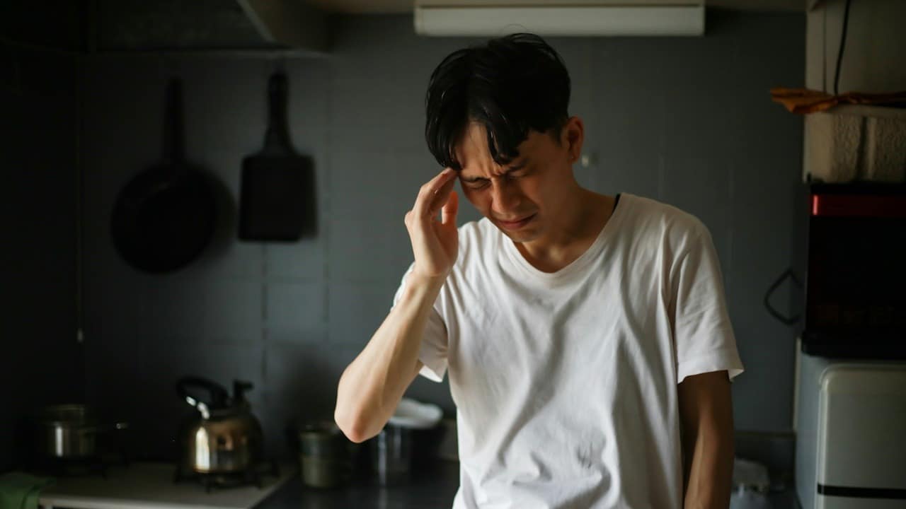 A man feeling a headache while he is standing in a kitchen.