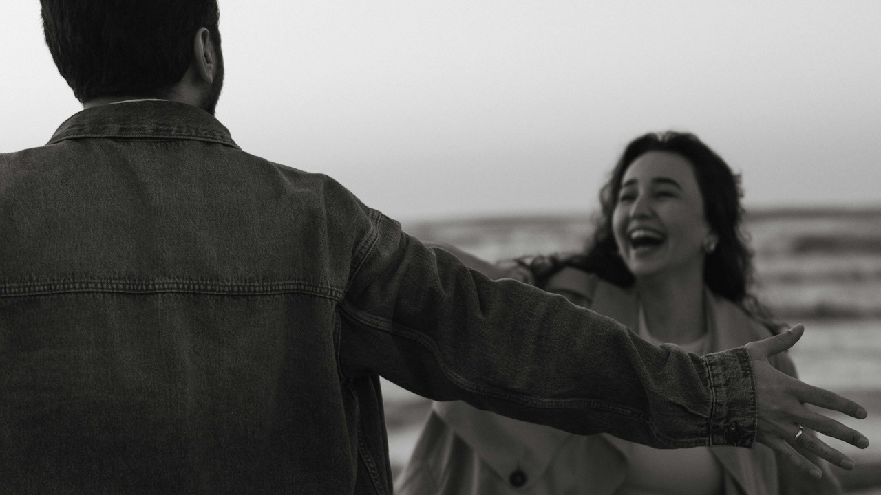 A man with open hands standing in front of a laughing woman who is coming towards him.