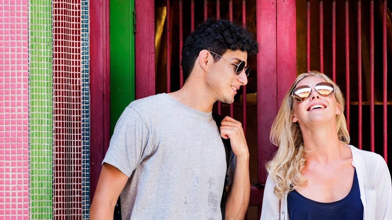 A man wearing sunglasses looking at a woman wearing sunglasses and smiling.