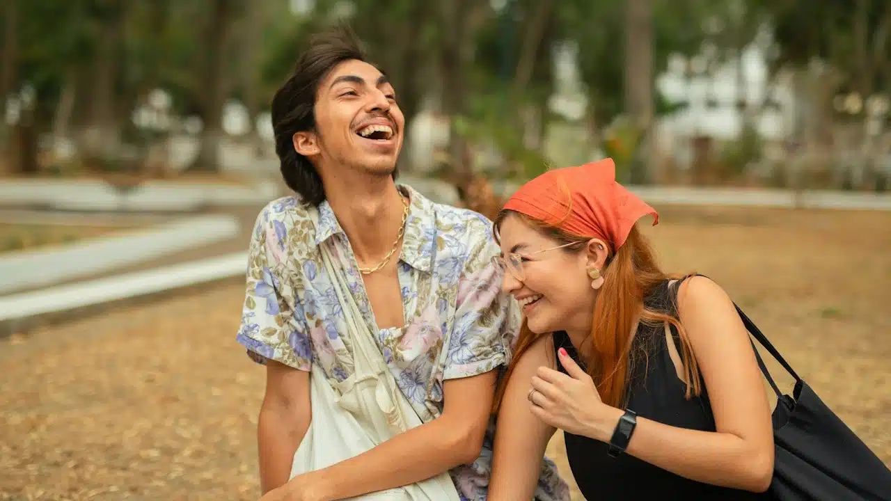 A cheerful young man and woman are sitting outdoors, laughing brightly together.