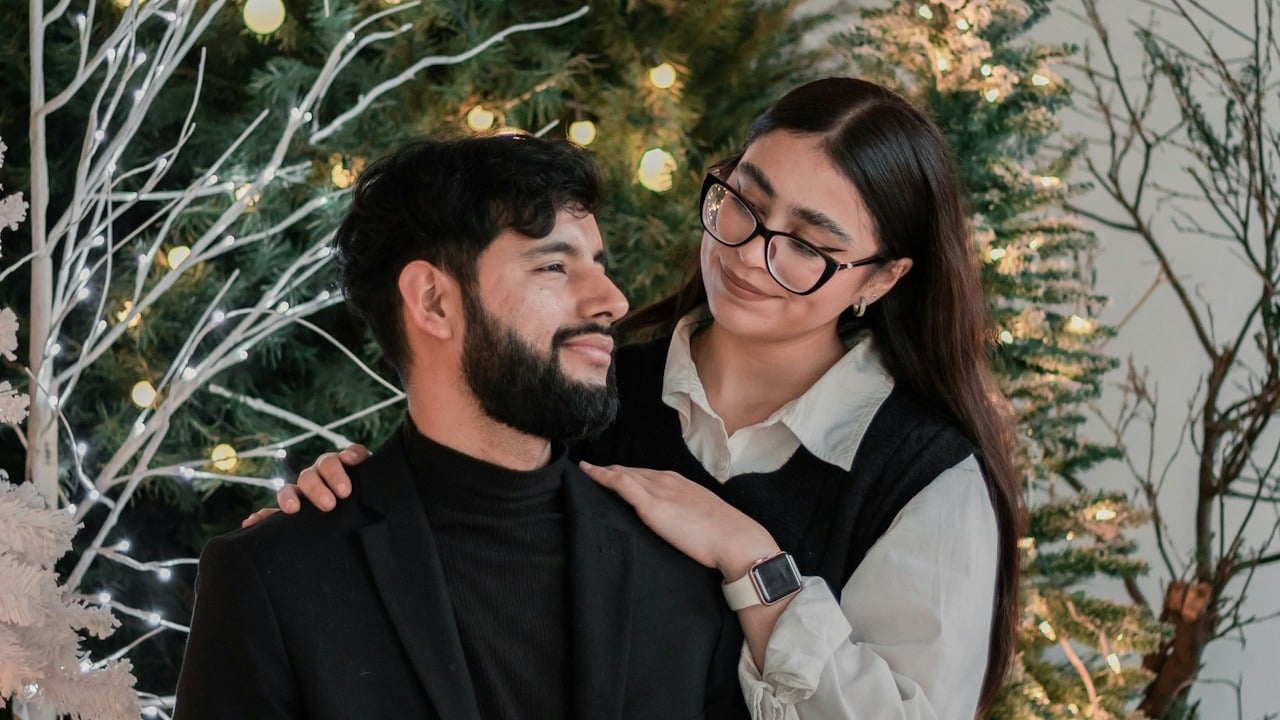 A couple posing for a picture in front of a Christmas tree.
