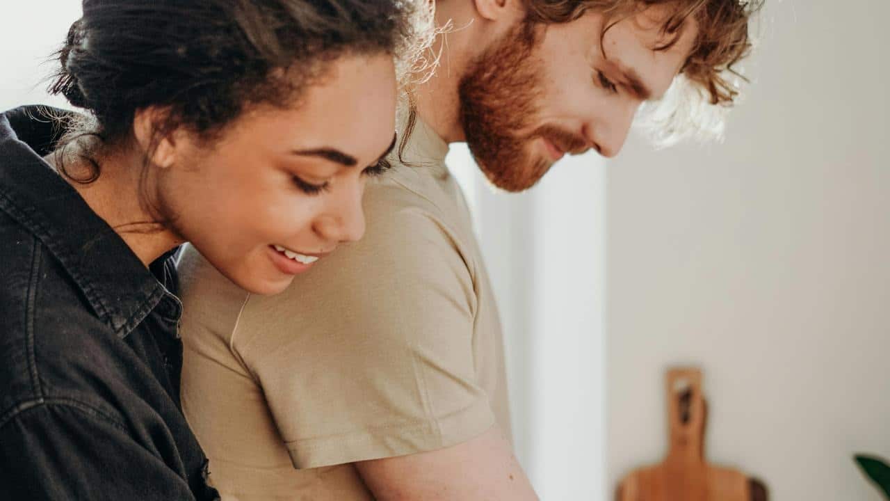 A woman hugging a man from behind while he mixes ingredients in a bowl.