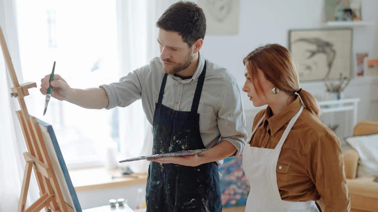 A man painting on a canvas while a woman watches beside him.