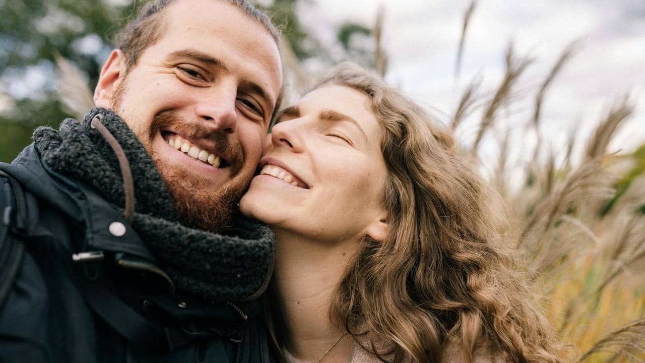 A couple smiling warmly while taking a selfie outdoors.
