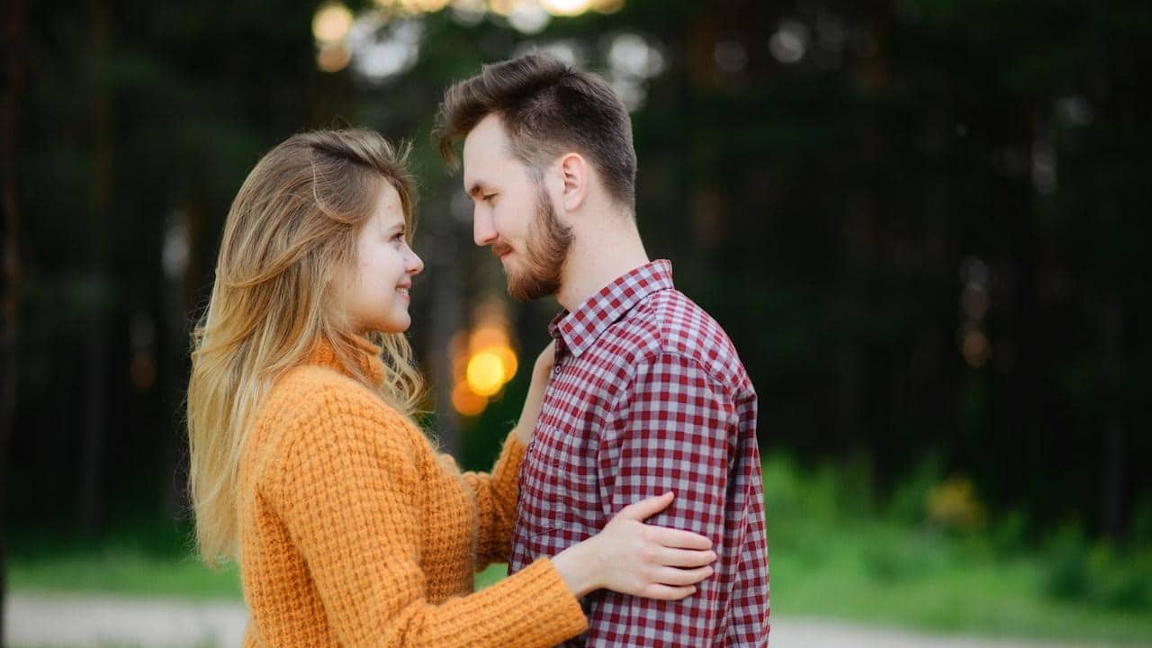 A man and woman facing each other while standing near a green field.