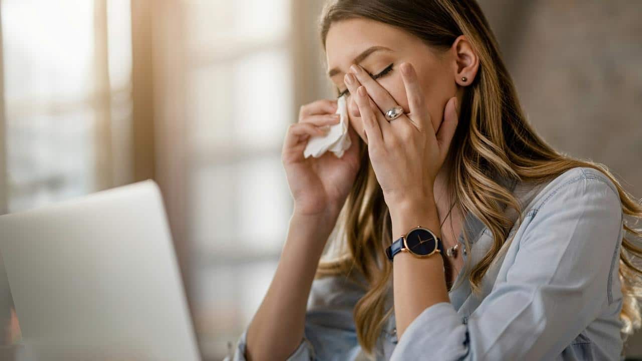 A woman sitting at a desk with a laptop wiping her eyes with a tissue.