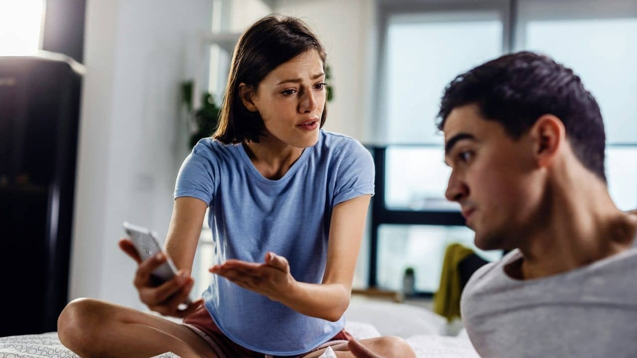 A woman gestures while holding a phone and arguing with a man sitting beside her.