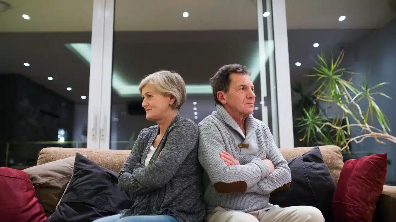 Couple sitting back-to-back on a couch, arms crossed, looking away from each other.