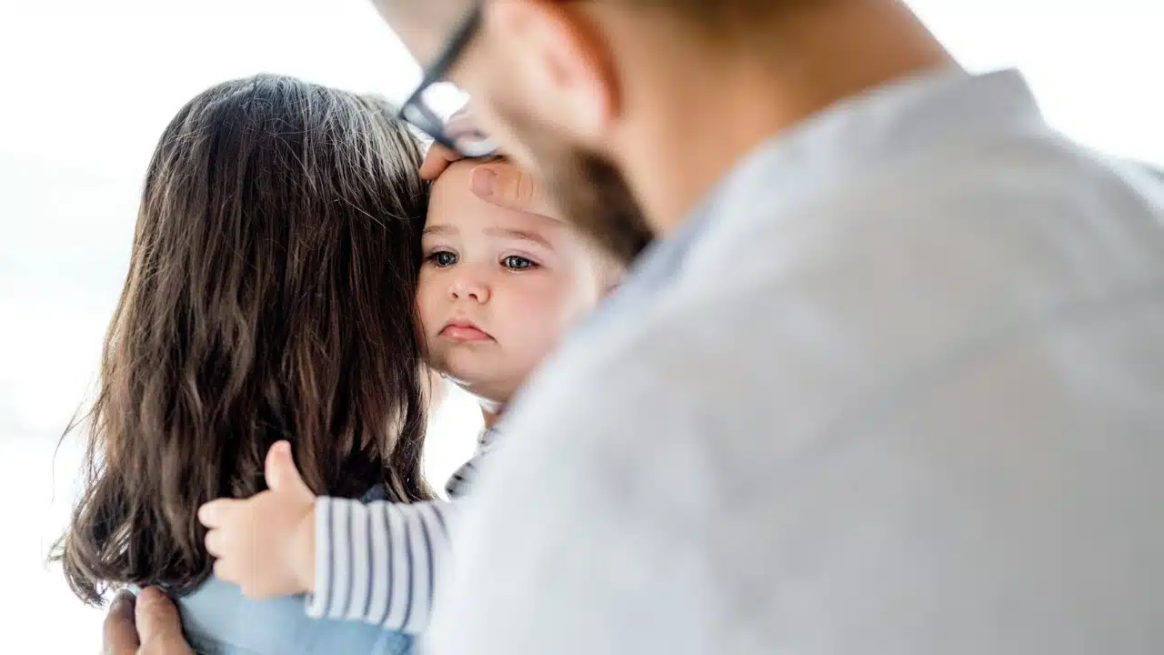 A man and woman embrace a small child who has a tear on their cheek.