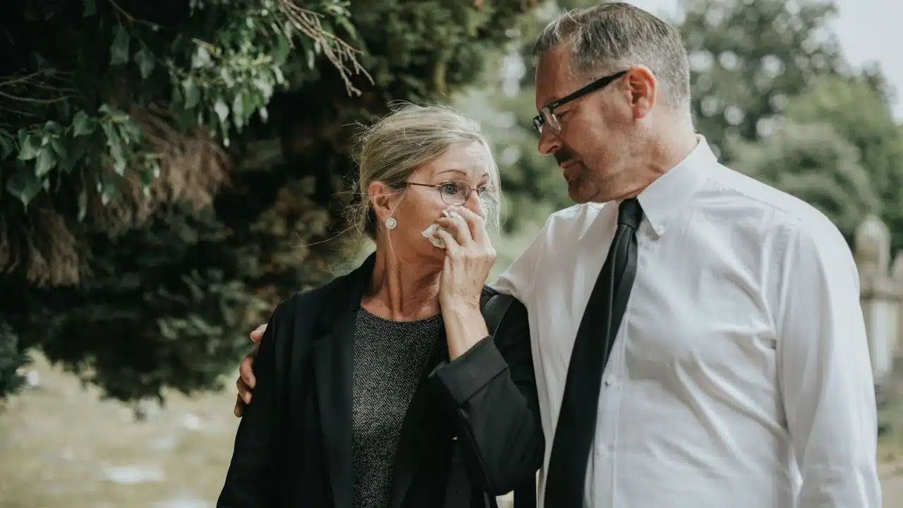 Man comforting a crying woman wiping her face with a tissue outdoors.