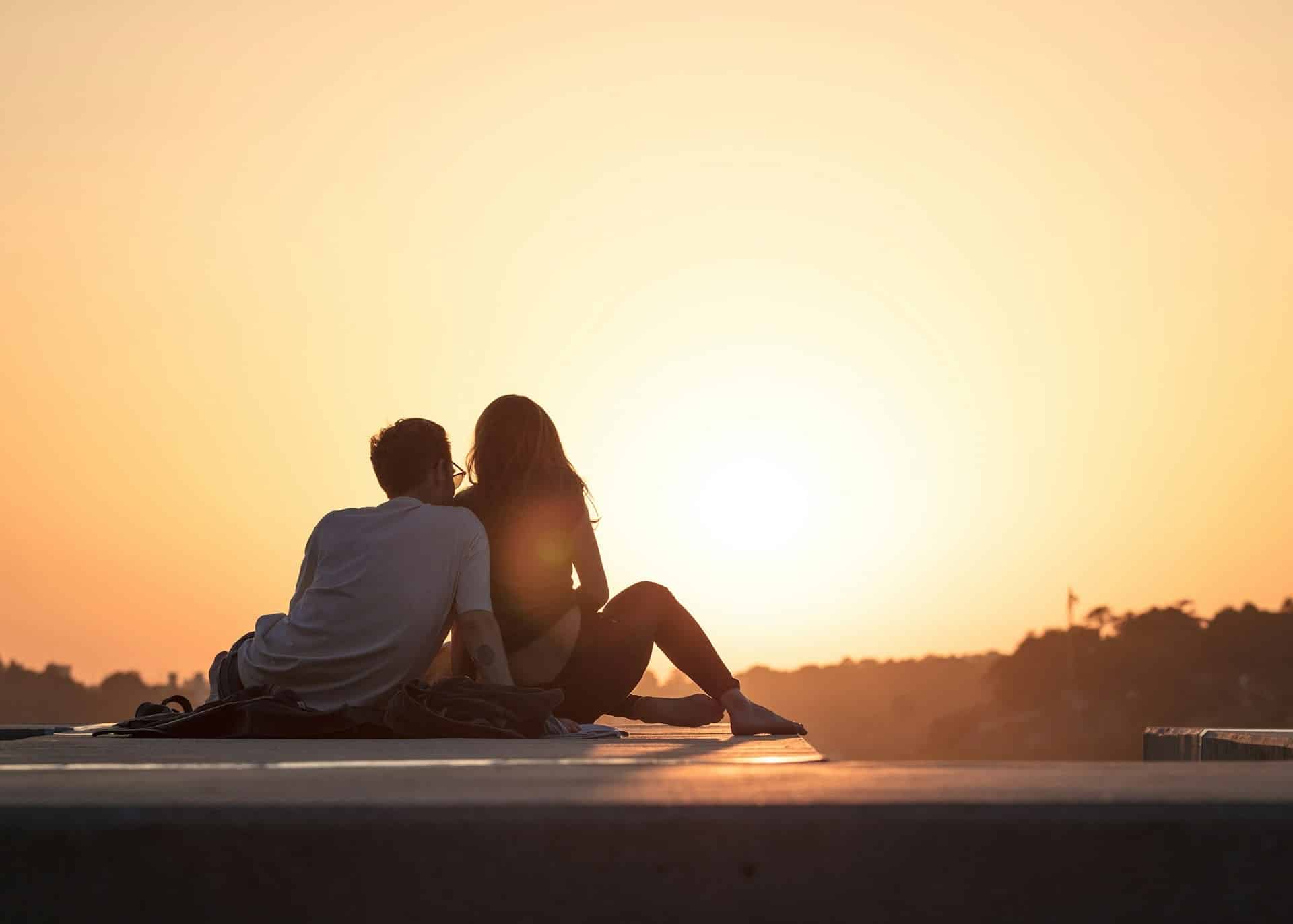 A couple sitting on a ledge watching the sunset together.