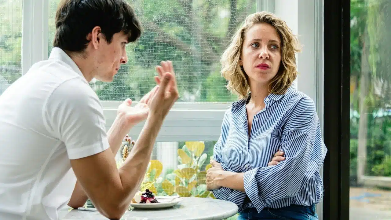 A woman with a look of disdain and contempt sits with her arms crossed while a man talks to her.