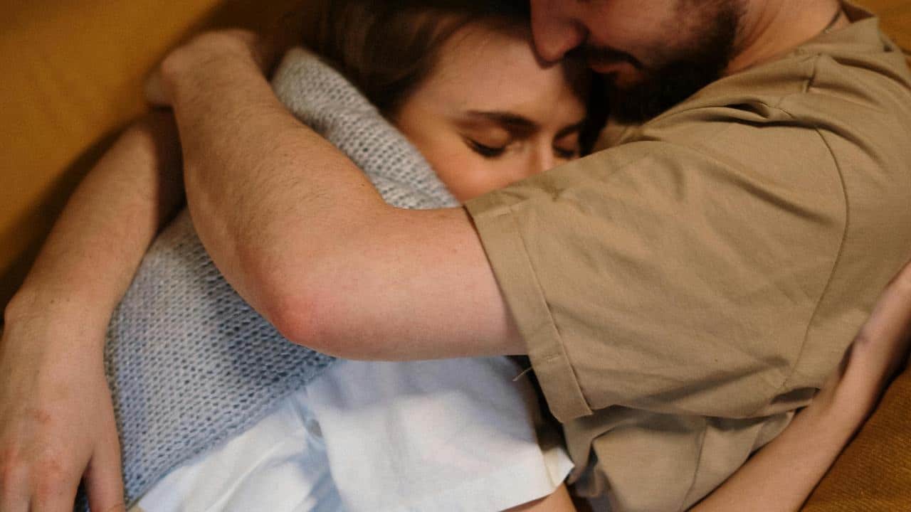 A couple hugging closely, with the woman’s eyes closed in comfort.