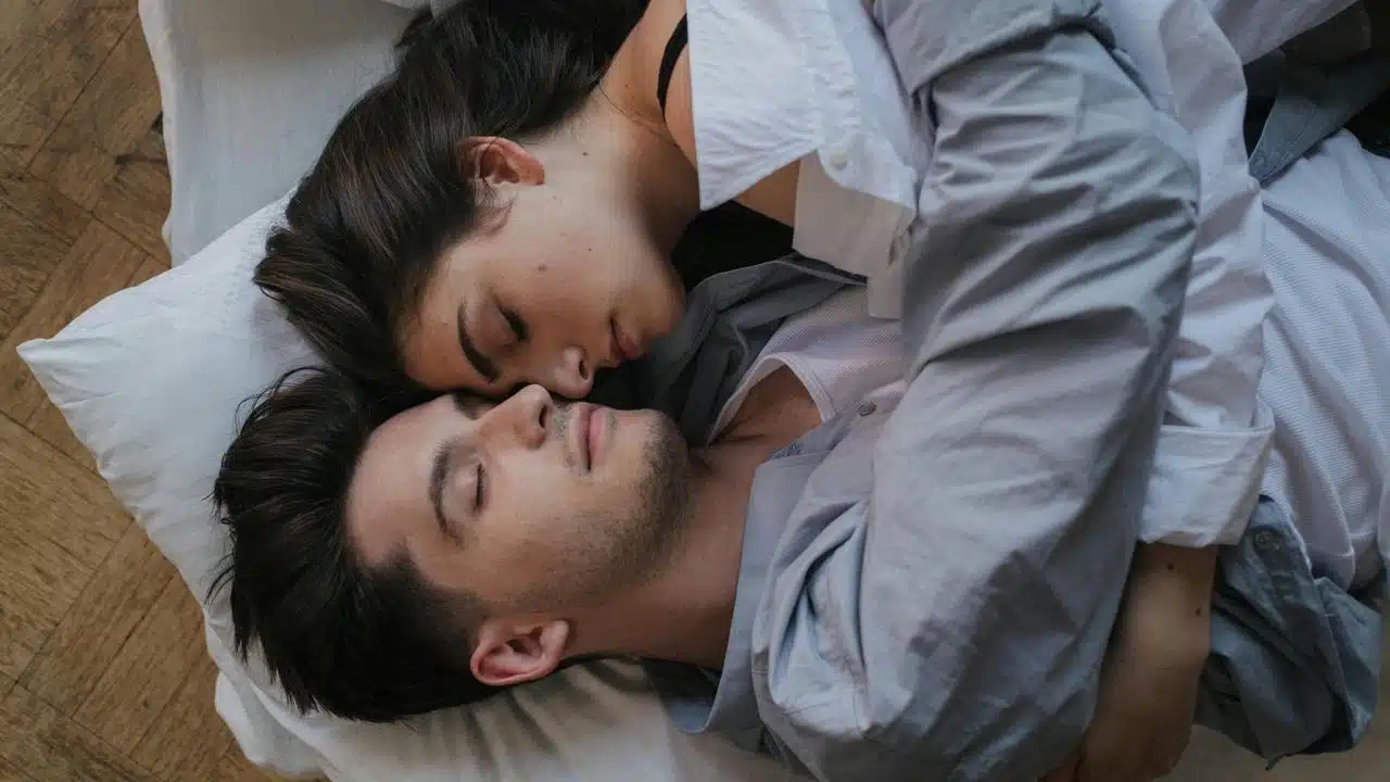 A couple lying closely together, peacefully resting with their eyes closed.