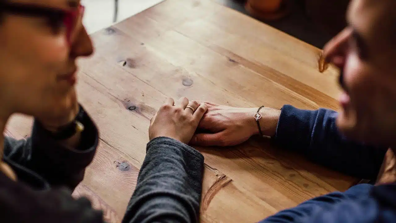 A couple holding hands across a wooden table affectionately.