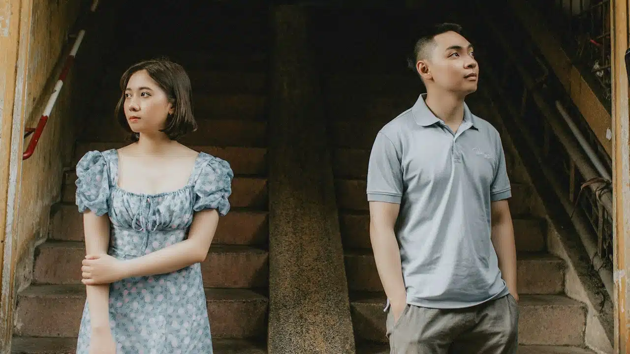 A couple standing apart at the base of some stairs and looking in opposite directions.